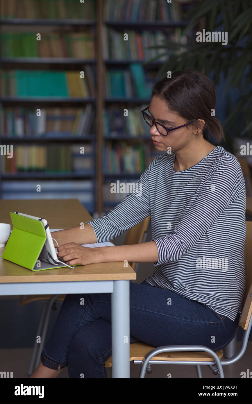 Female university student using digital tablet while studying at desk in classroom Stock Photo