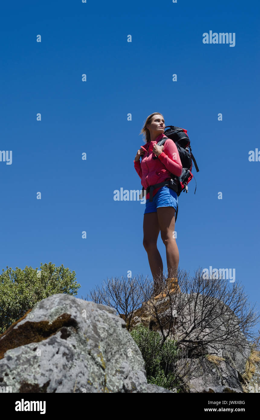 Low angel view of female hiker standing on rock against clear blue sky Stock Photo
