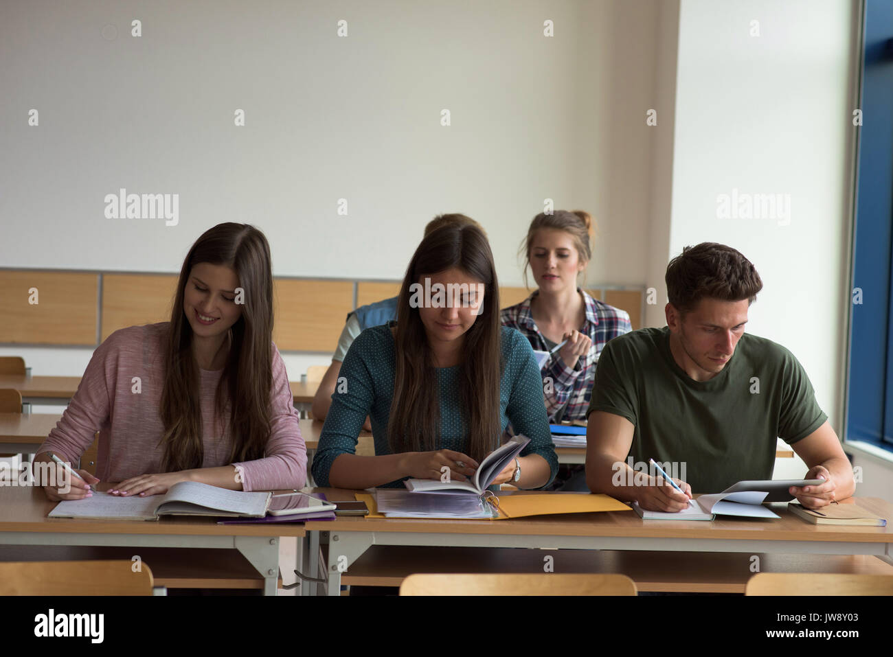 Young College Students At Desks By Window In Classroom Stock Photo