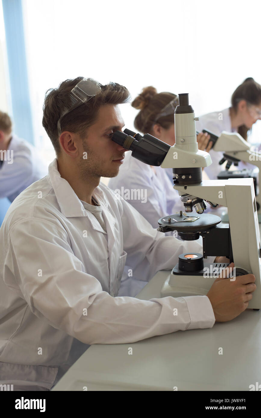 College students using microscope while practicing experiment in lab