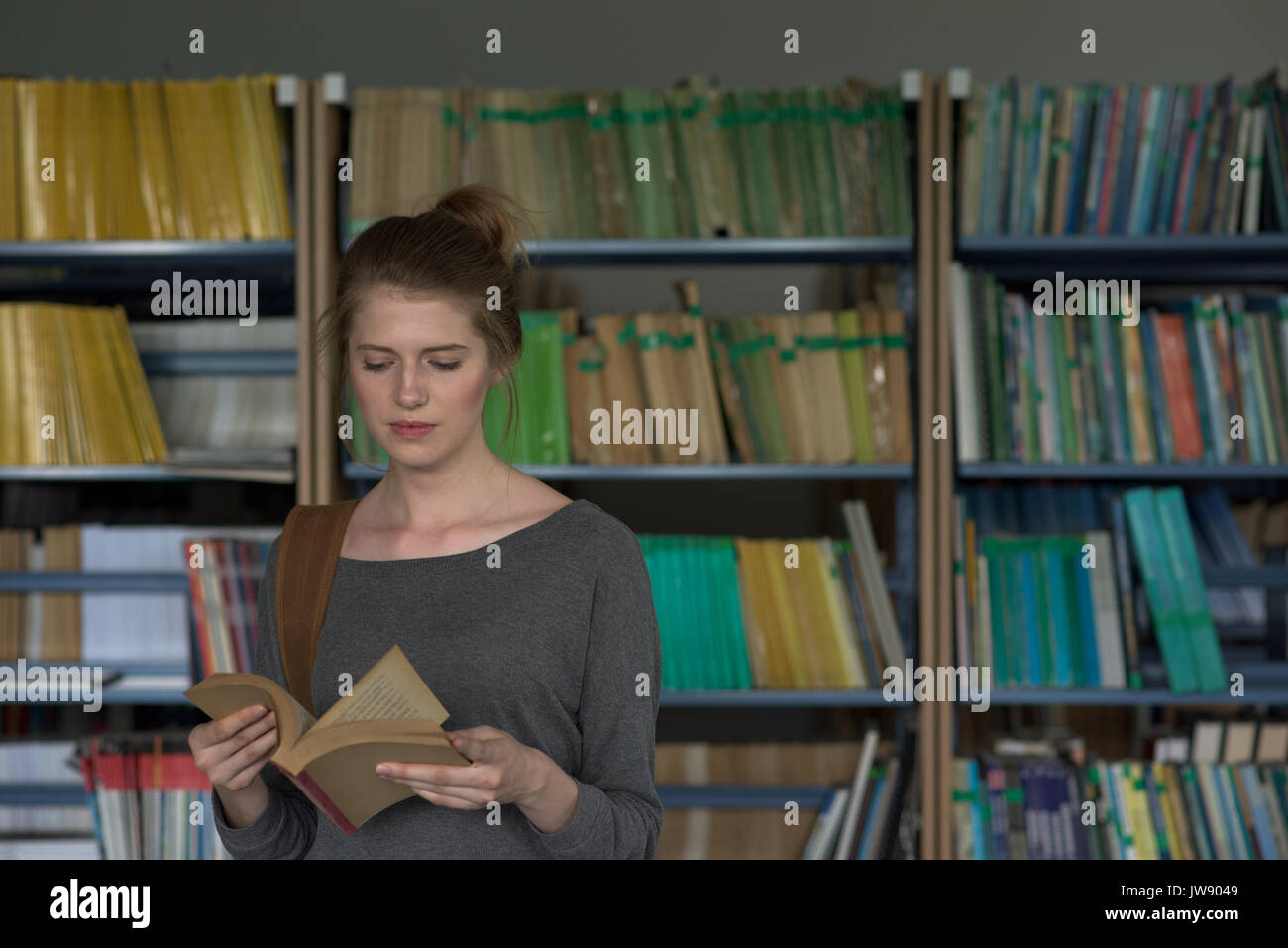 Young female student reading book while standing in library Stock Photo