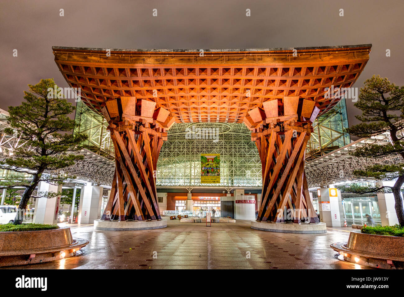 Landmark Tsuzumi gate, aka drum gate, at Kanazawa station, Japan. Night time after rain. View through gate to glass Motenashi dome. Few people Stock Photo