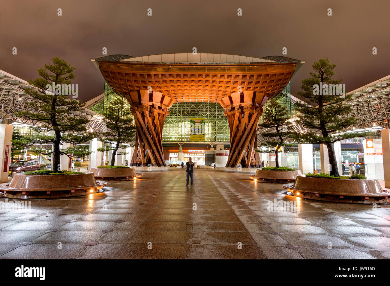 Landmark Tsuzumi gate, aka drum gate, at Kanazawa station, Japan. Night time after rain. View through gate to glass Motenashi dome. Few people Stock Photo