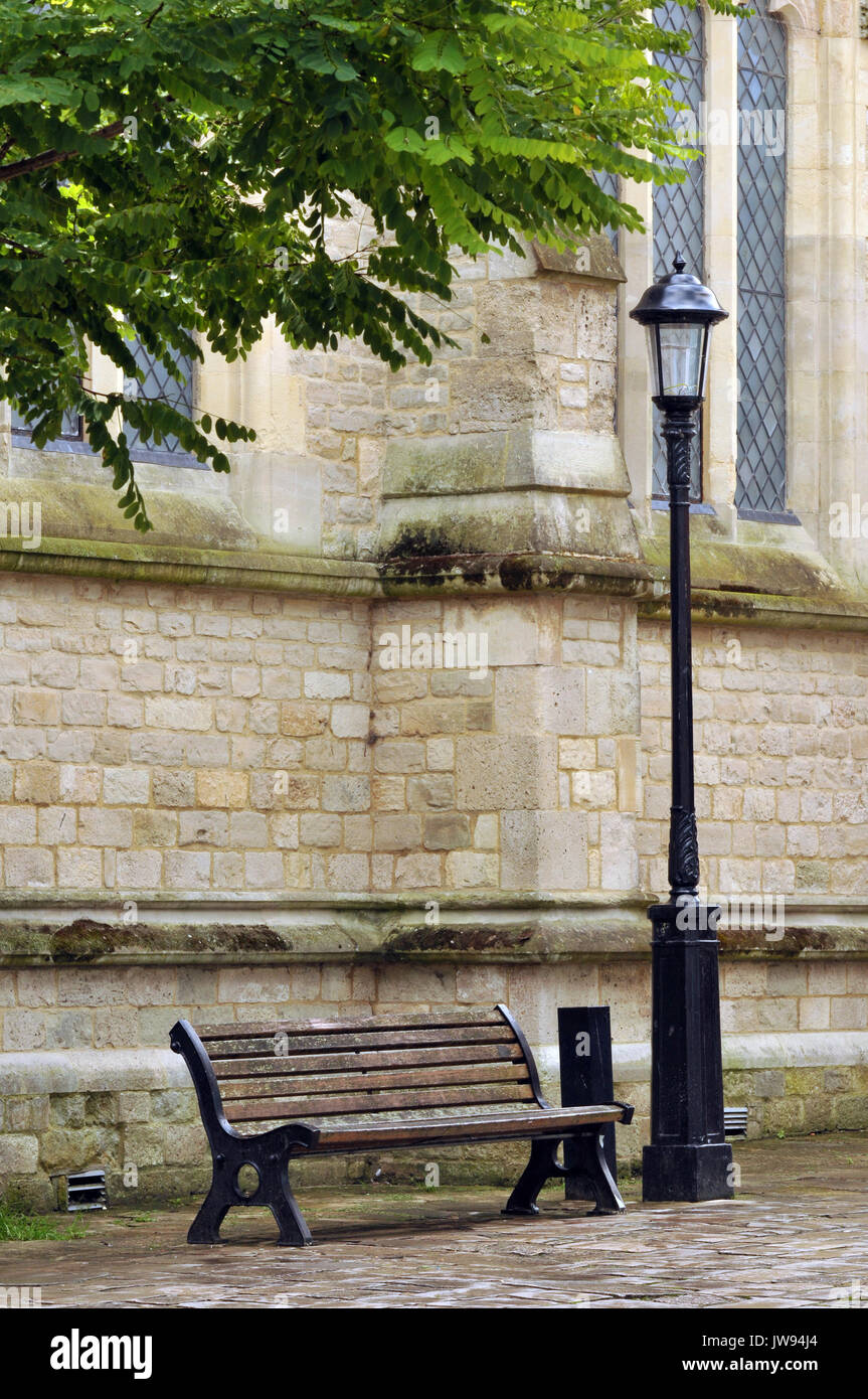 a wooden bench and victorian lamppost at the side of a stone wall 