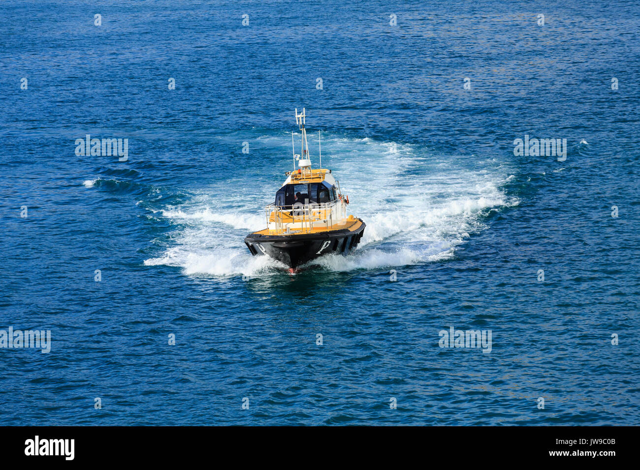 A black and yellow pilot boat cutting through the blue water of Barcelona harbor Stock Photo