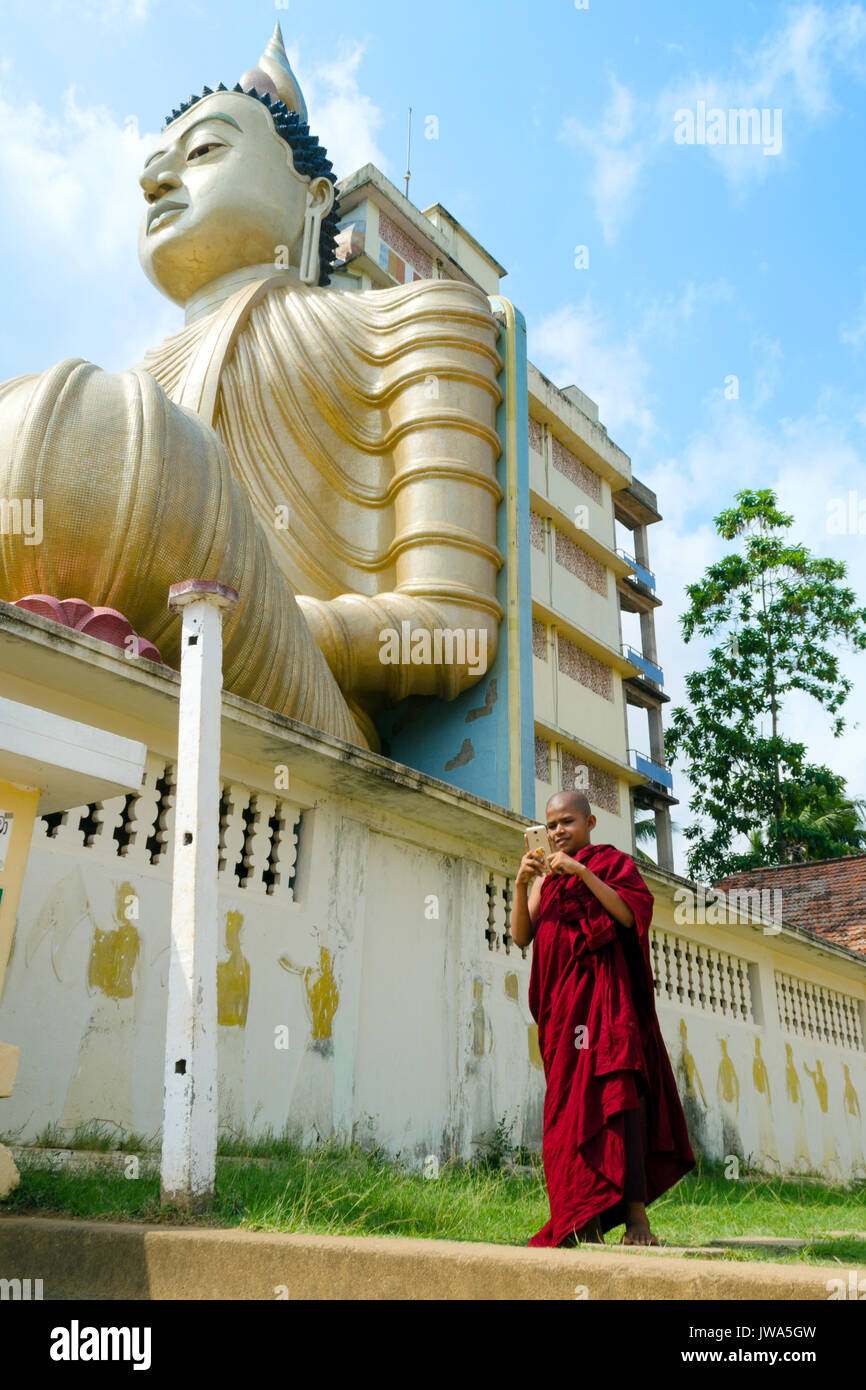 Dickwella, Sri Lanka, 04-15-2017: A Buddhist monk holds a mobile phone in the hands of a Buddhist temple on the background of a Buddha statue Stock Photo