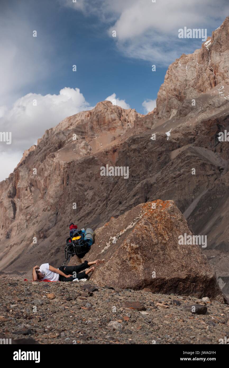 Side view of young climber having a rest during fatiguing mountain hiking day. Kokshaal-Too Tien-Shan mounitans, Kyrgyzstan. Central Asia. Stock Photo