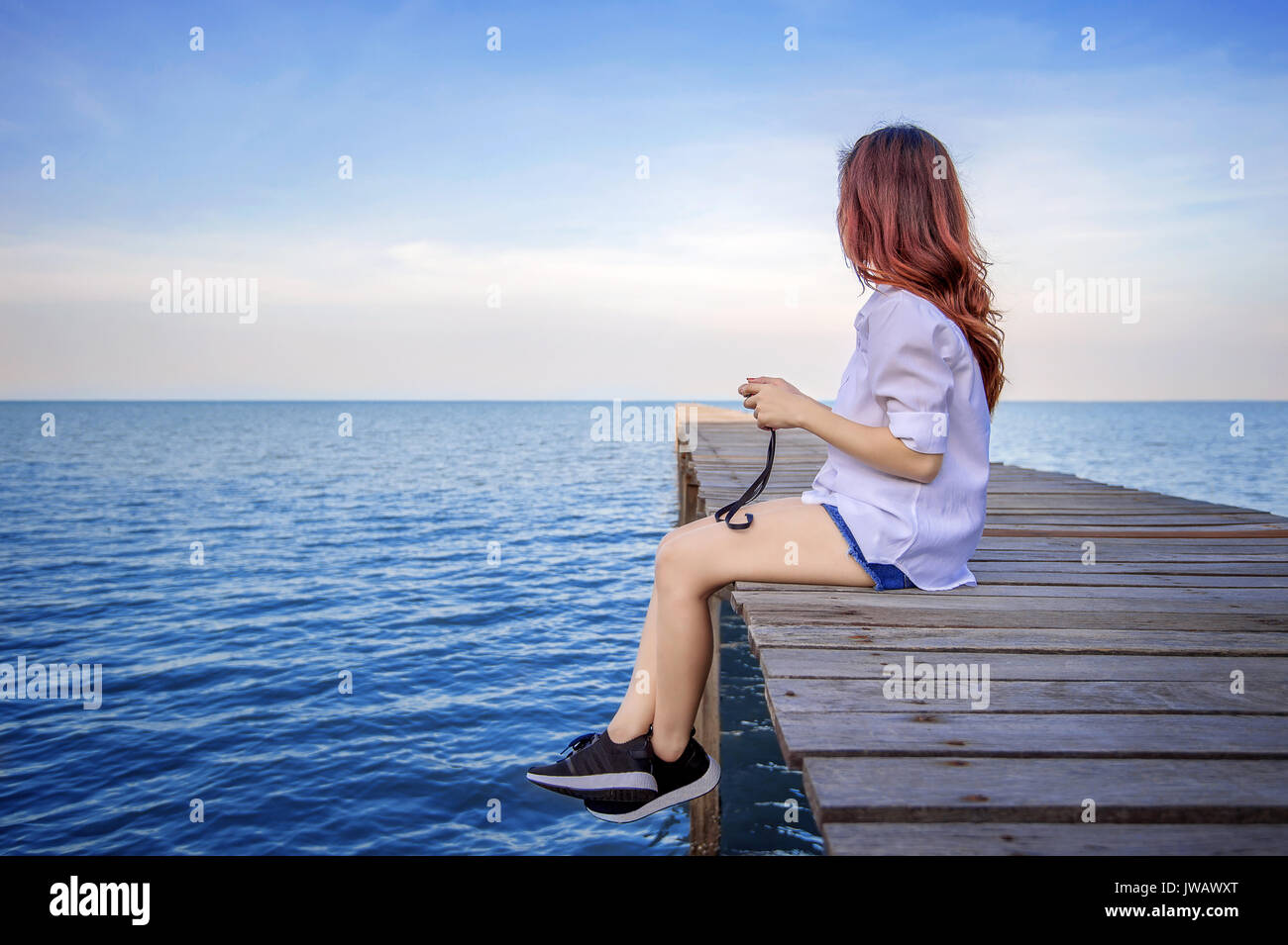 Girl sitting alone on a the wooden bridge on the sea. Vintage tone style. Stock Photo
