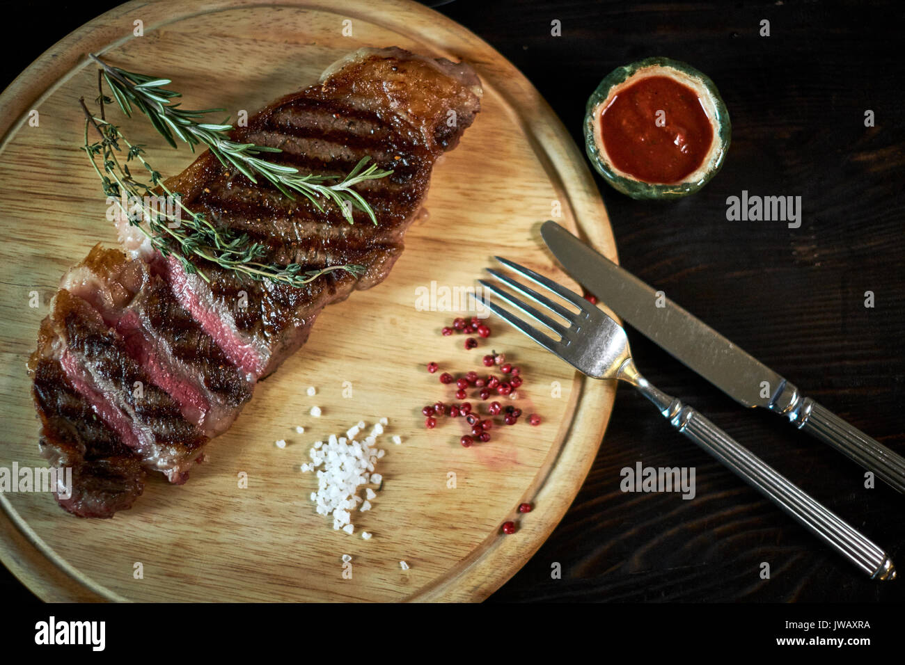Sliced medium rare grilled steak on rustic cutting board with rosemary and spices , dark rustic metal background, top view, place for text Stock Photo