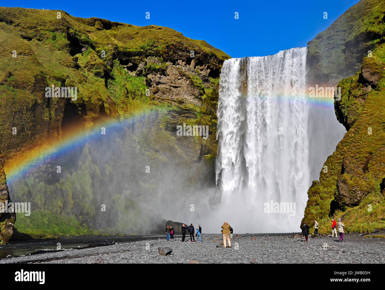 Skogafoss waterfall and rainbow with incidental tourists. Skogafoss is a waterfall situated on the Skoga River in the south of Iceland at the cliffs o Stock Photo
