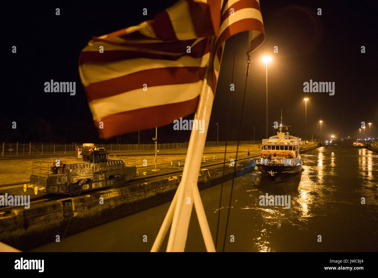 As the American flag bellows in the wind,a vessel and cruise ship are guided through the Gatun Locks of the Panama Canal. Stock Photo