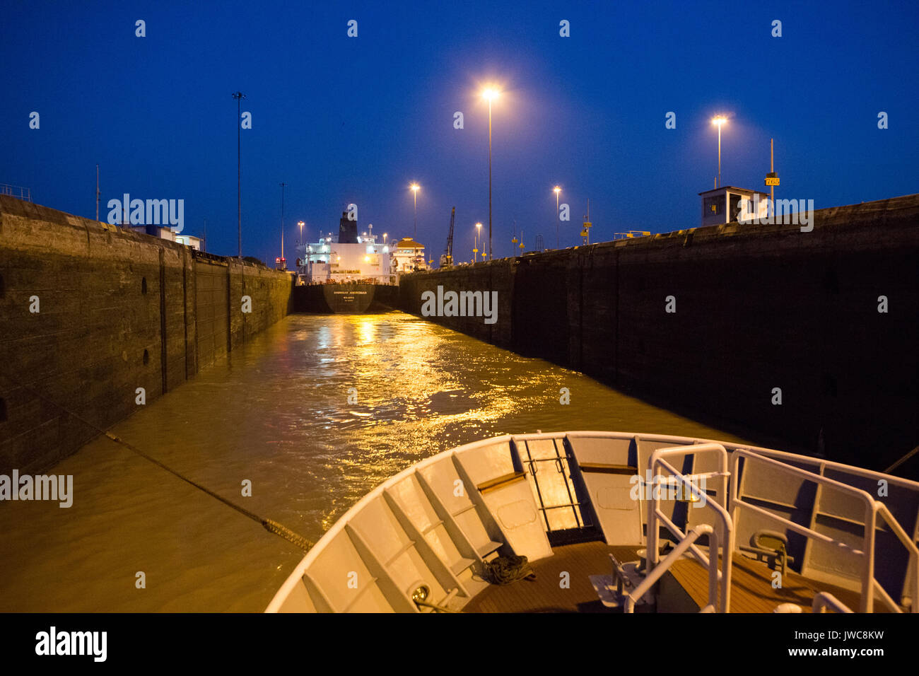 A large shipping vessel and expedition cruise ship are guided through the Pedro Miguel Locks in the Panama Canal. Stock Photo