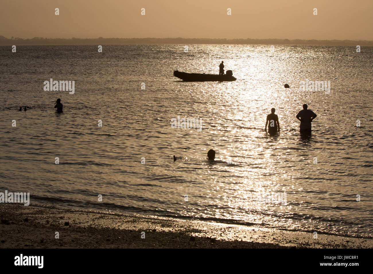 As the sun sets over the waters near Iguana Island,Isla Iguana,a man in an inflatable boat watches travelers stand in the water. Stock Photo