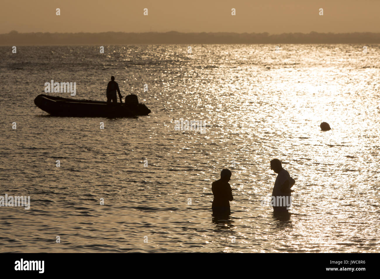 As the sun sets over the waters near Iguana Island,Isla Iguana,a man in an inflatable boat watches travelers stand in the water. Stock Photo