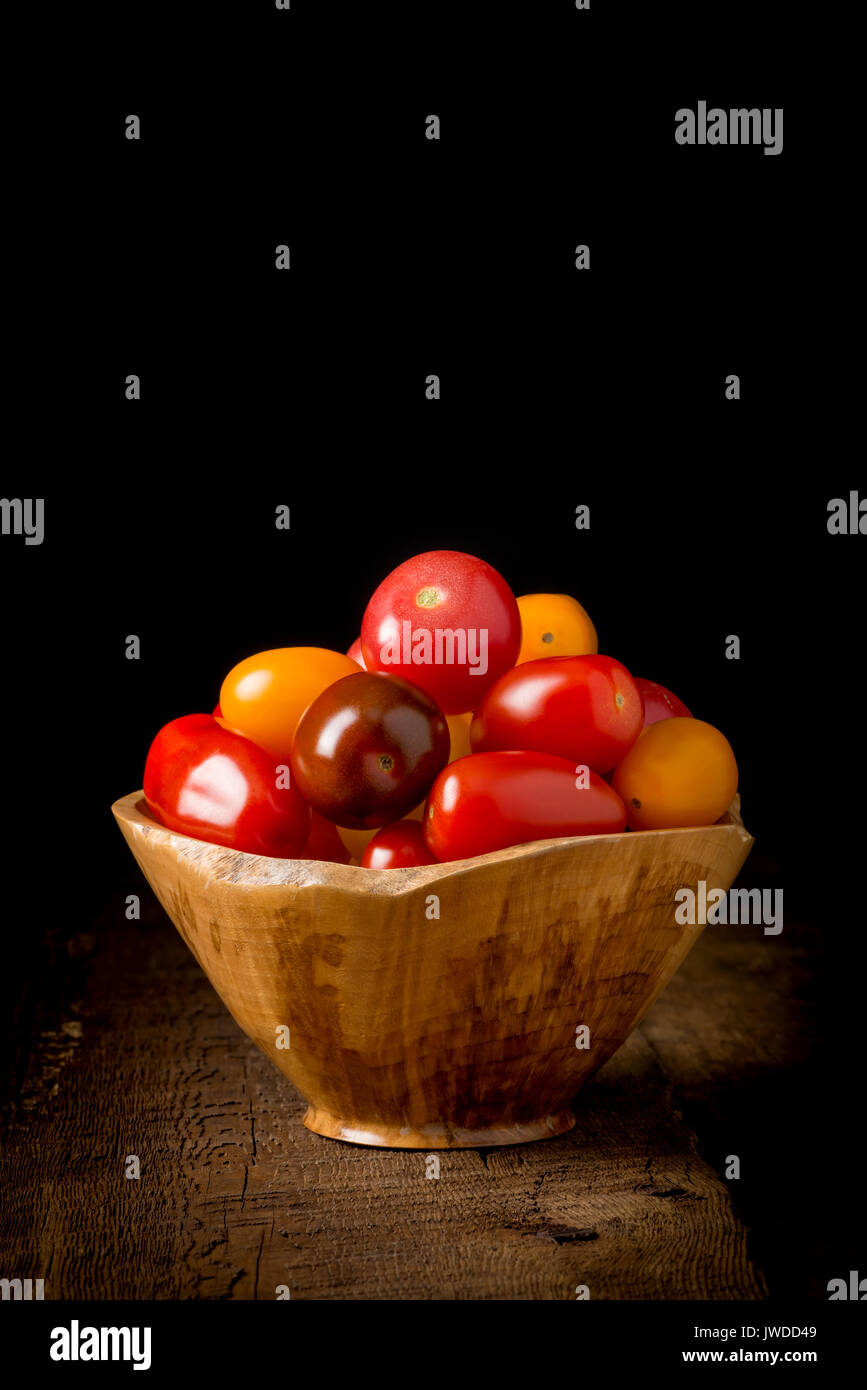 Bowl of fresh heirloom tomatoes on a low key rustic background.  May be suitable for food services promotional materials. Stock Photo