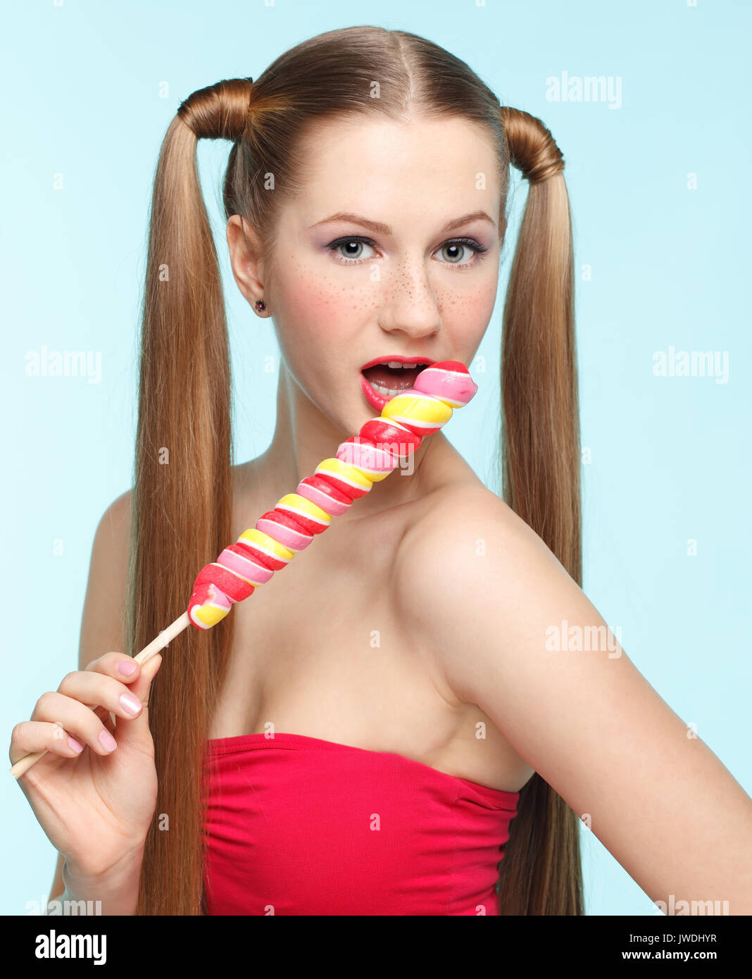 Beautiful playful young freckled girl licking lollipop on blue background Stock Photo
