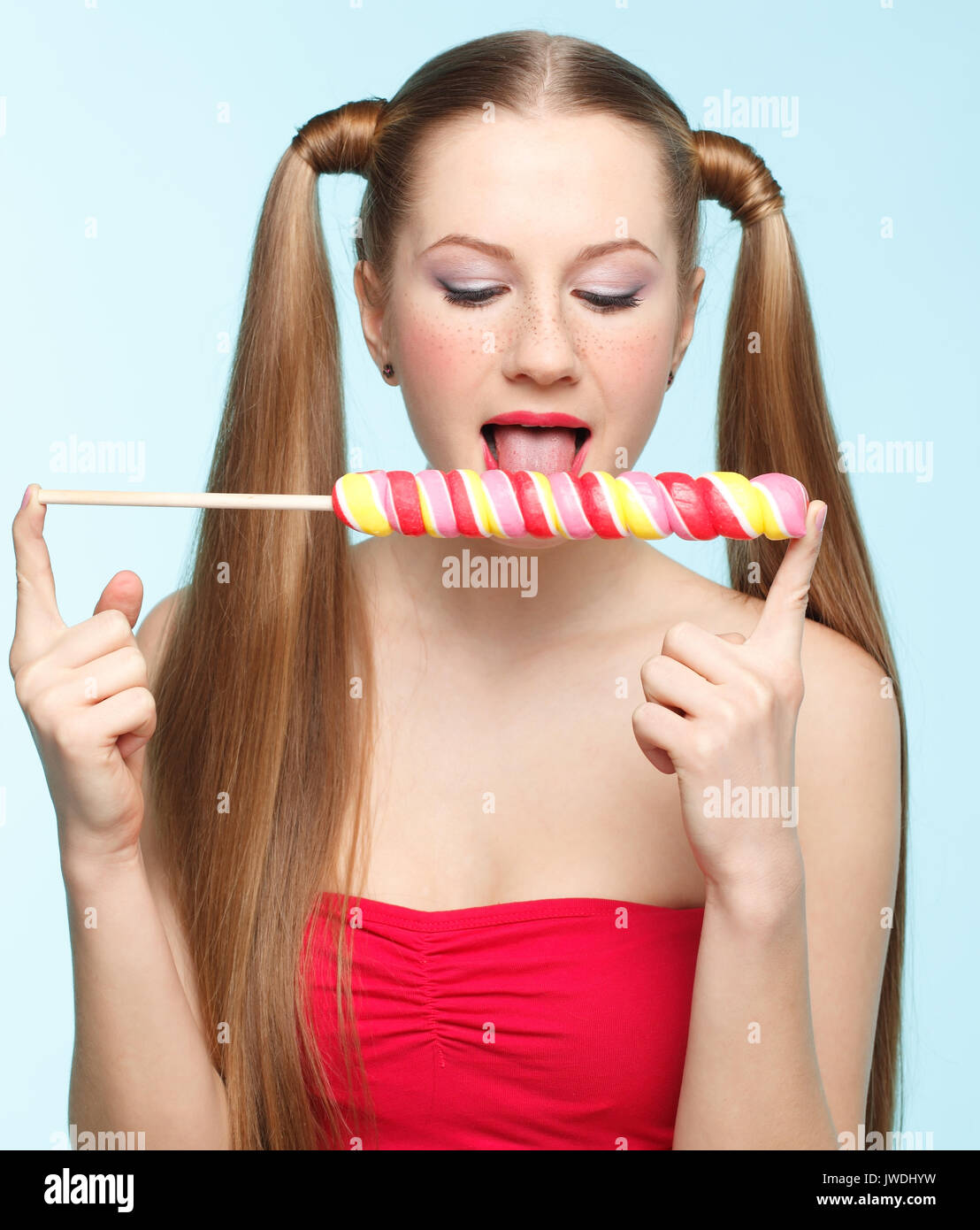 Beautiful playful young freckled girl licking lollipop on blue background Stock Photo
