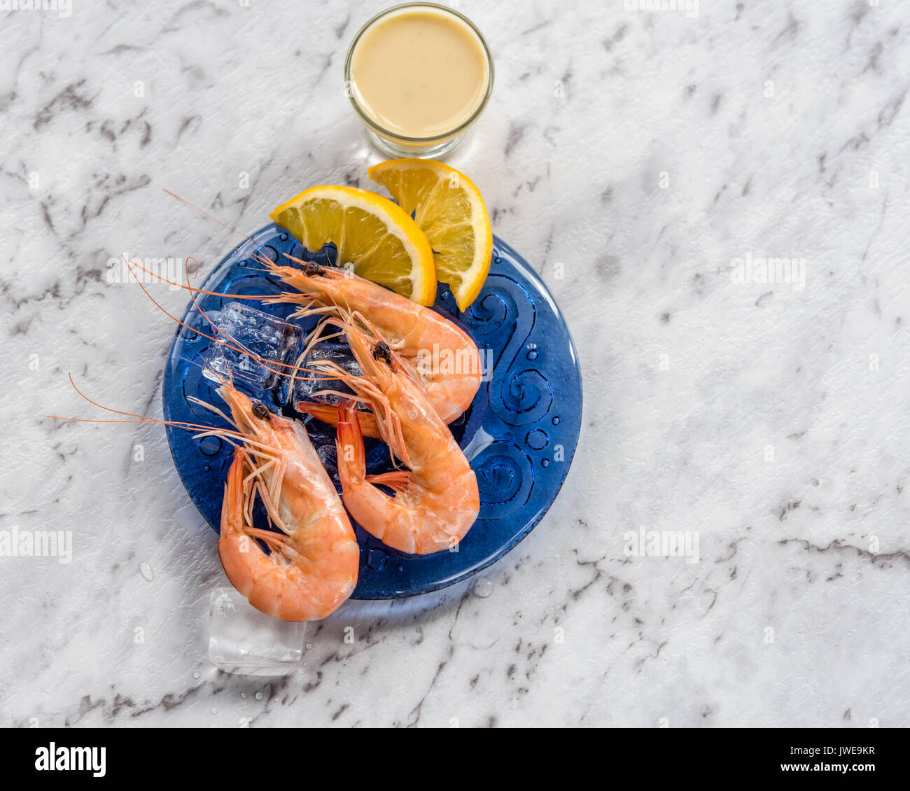 Shrimp on blue plate with sauce white marble background.  Prawn on blue plate with sauce, ice, lemon slices, white marble background. Stock Photo