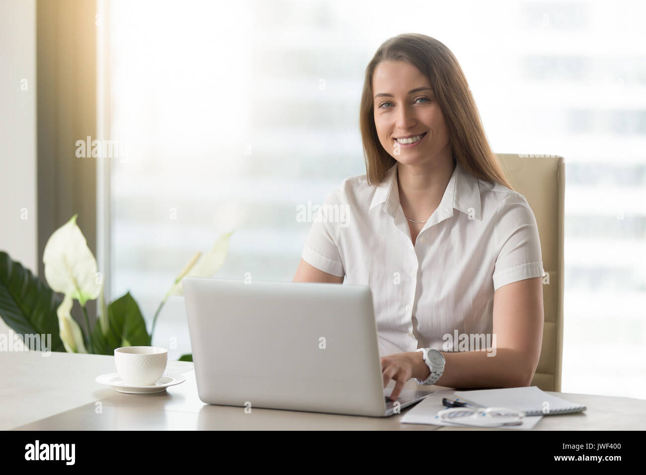 Pretty businesswoman working on laptop, smiling for camera at wo Stock Photo