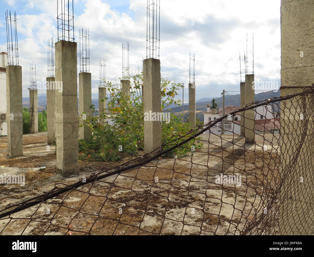Abandoned building site with tall Reinforced concrete pillars behind rusty fence Stock Photo