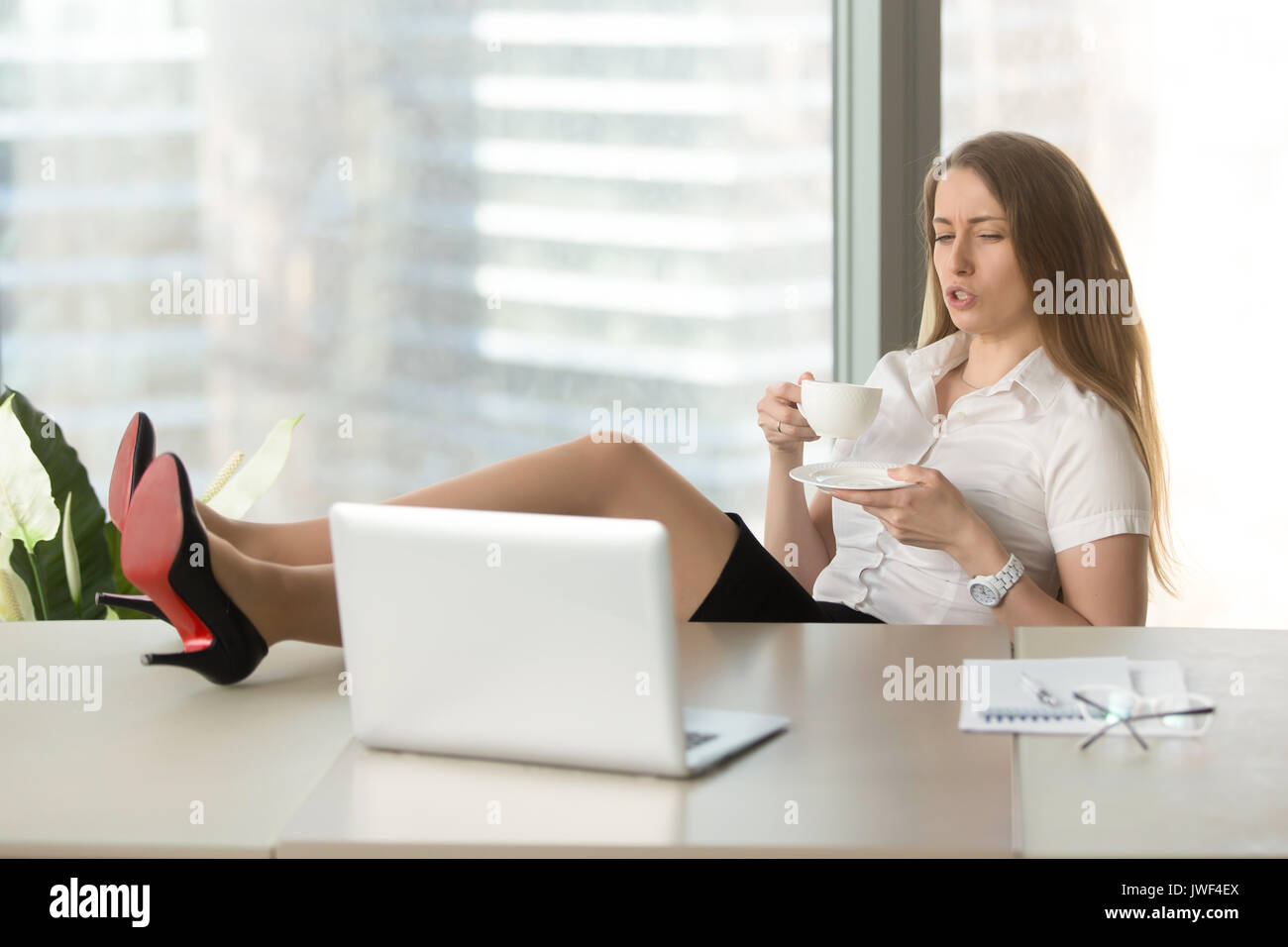 Relaxed businesswoman lazy to work drinking coffee, feet on desk Stock Photo