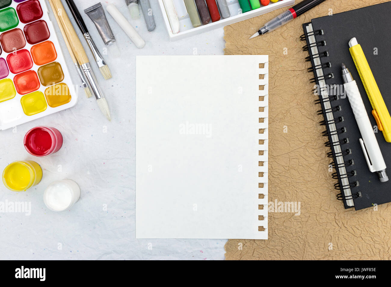 artistic work tools: watercolor palette, various paintbrushes, colored chalks and sketchbook. artist workplace. Stock Photo