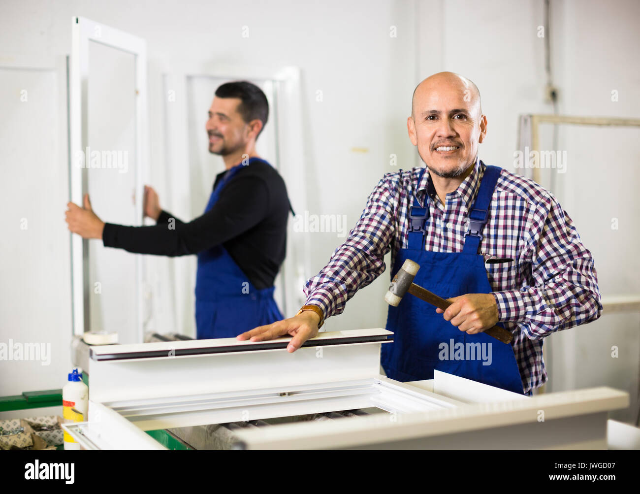 Two smiling professional workers in blue coverall with different PVC windows and doors Stock Photo