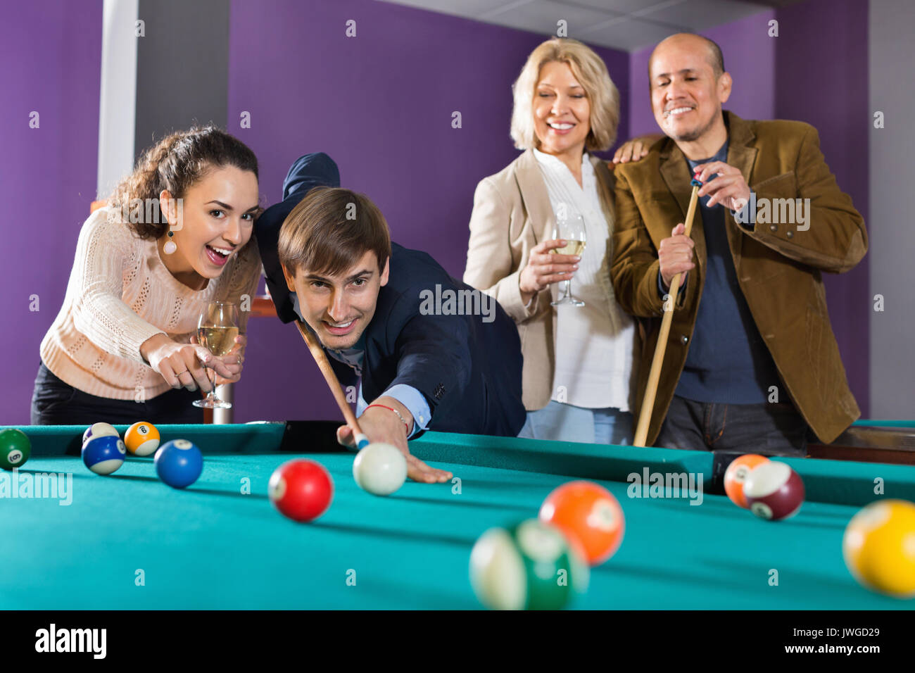 Group of positive friends playing billiards and smiling in night club