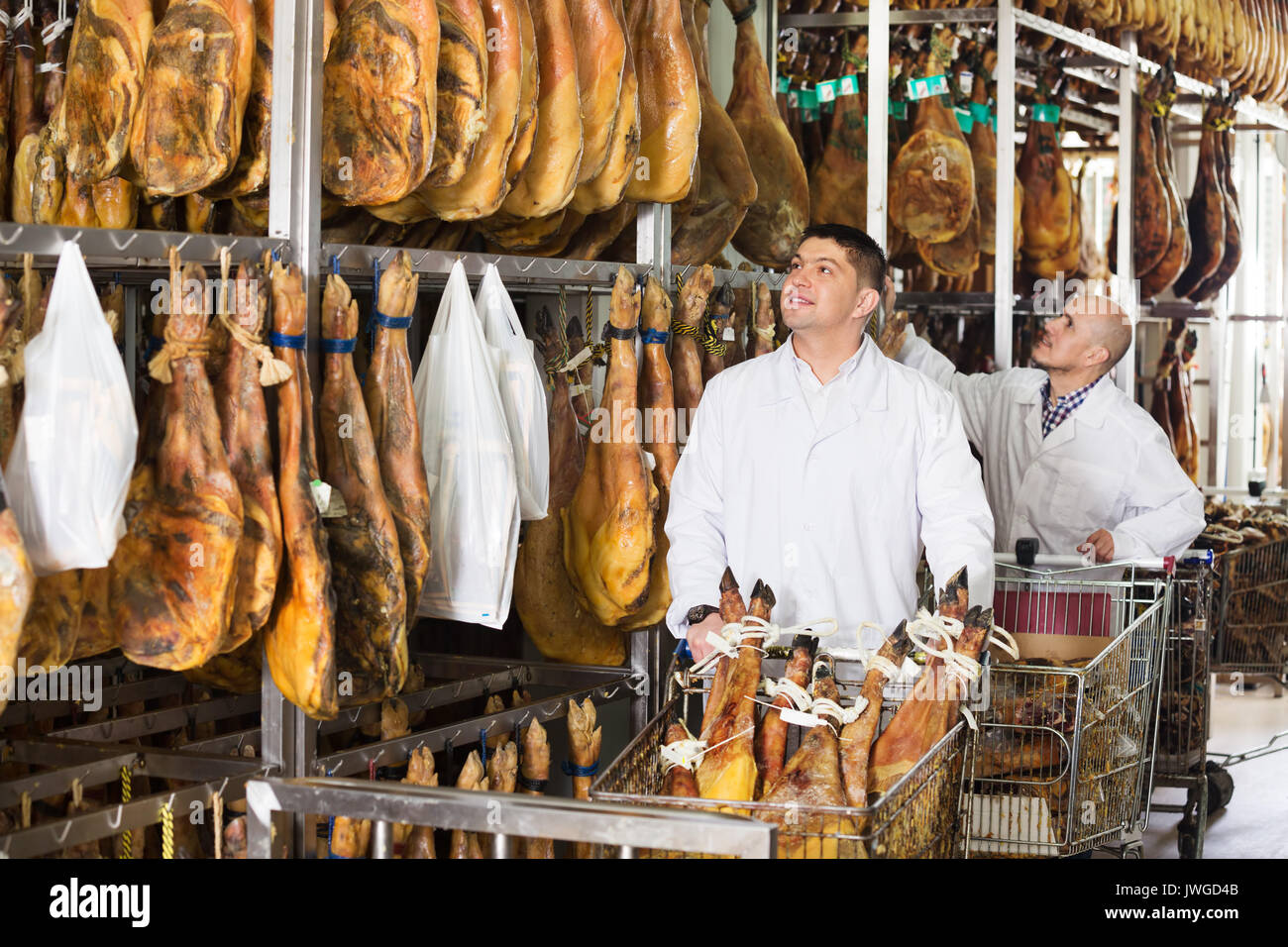 Mature butcher and his assistant with the jamon joints at meat factory