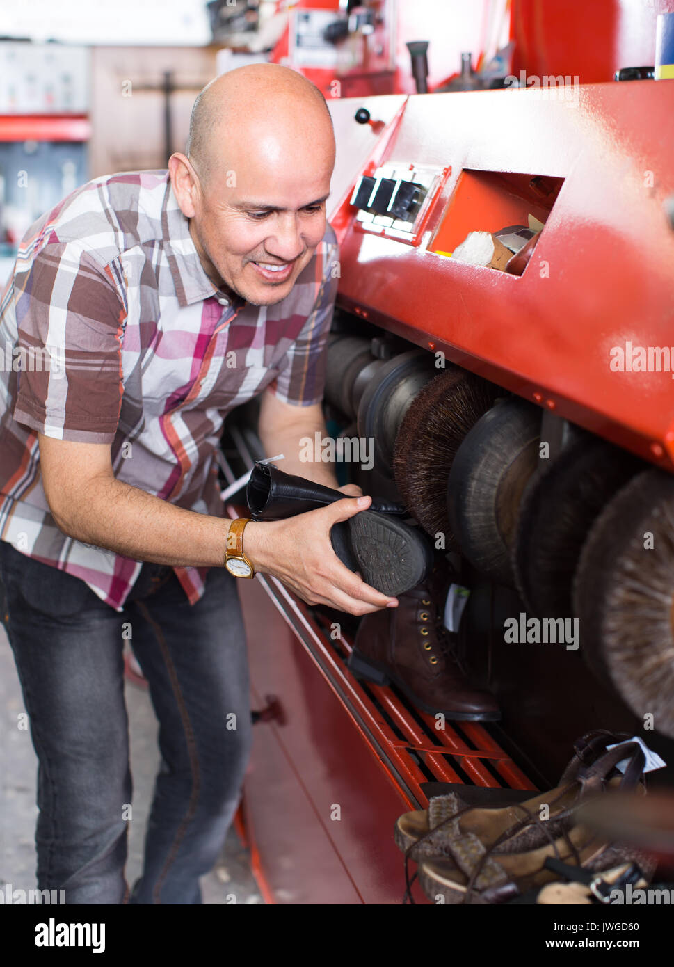 Mature workman giving leather boots a high polish in Stock