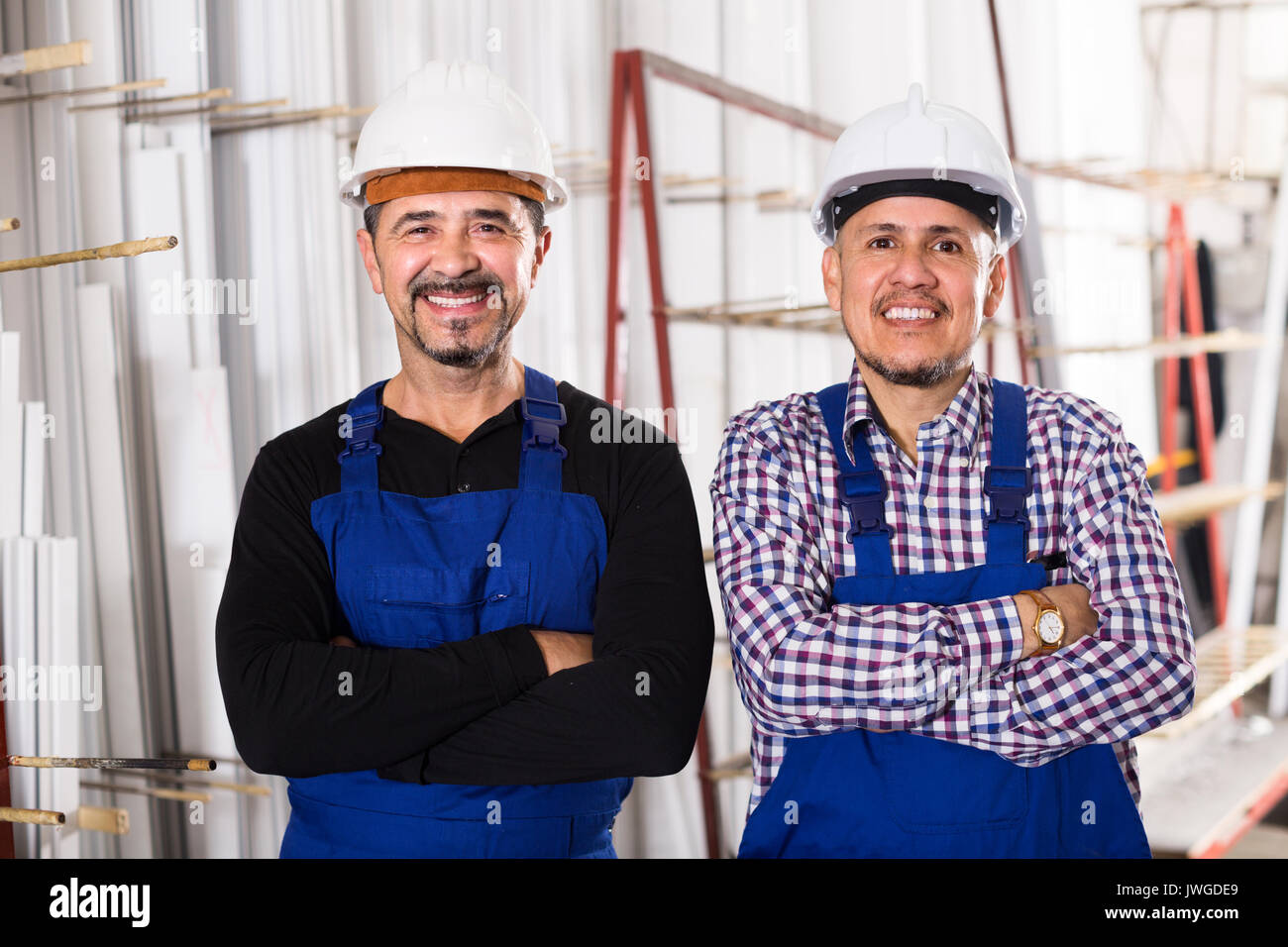 Two positive specialists in helmets and workwear posing at workshop Stock Photo