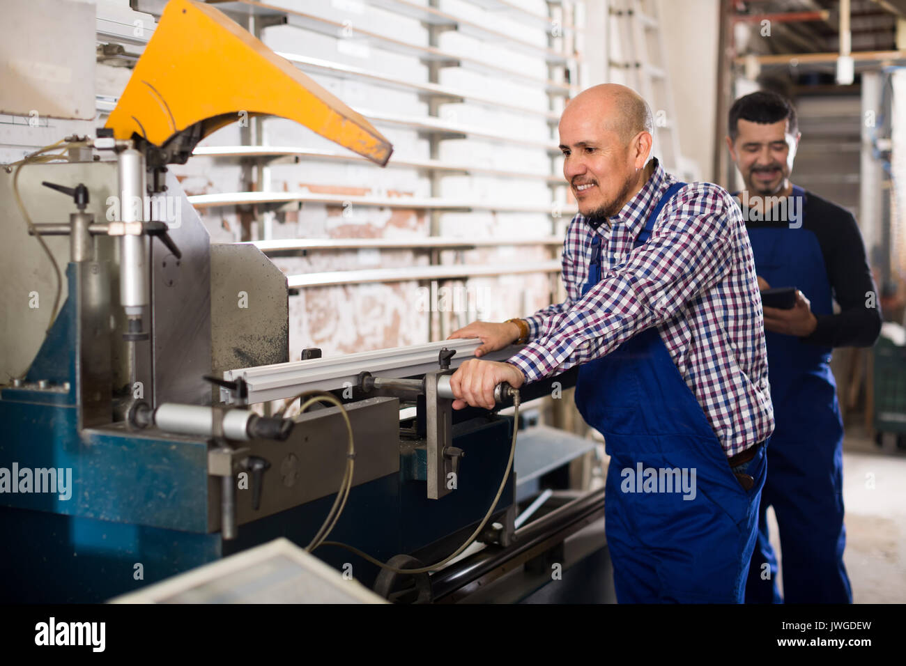 Couple of positive workmen in overalls near cutter - lathe machine at factory Stock Photo