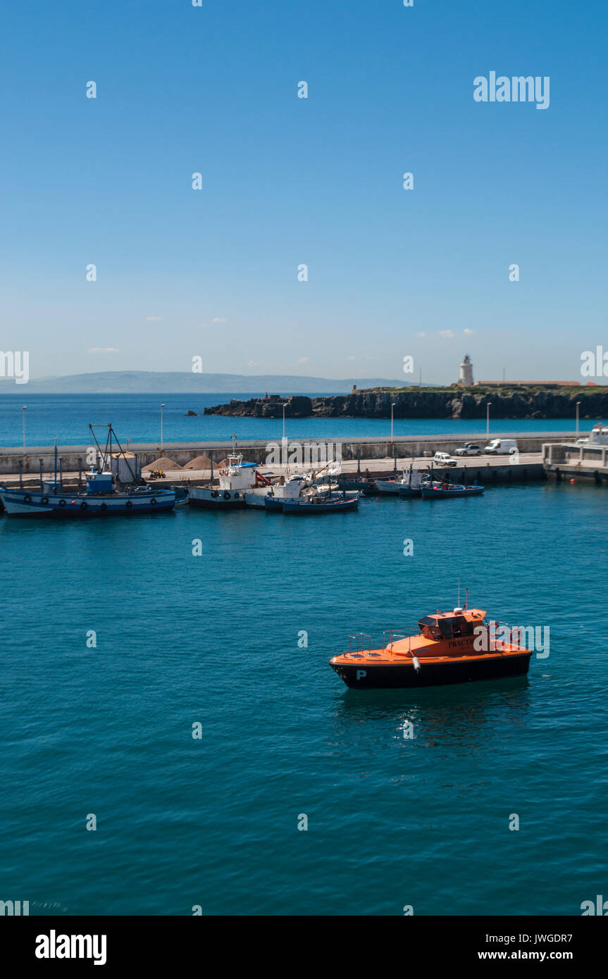 A boat in the port of Tarifa, facing the Strait of Gibraltar and Morocco, with the the lighthouse of Punta de Tarifa (Point Tarifa) in the background Stock Photo