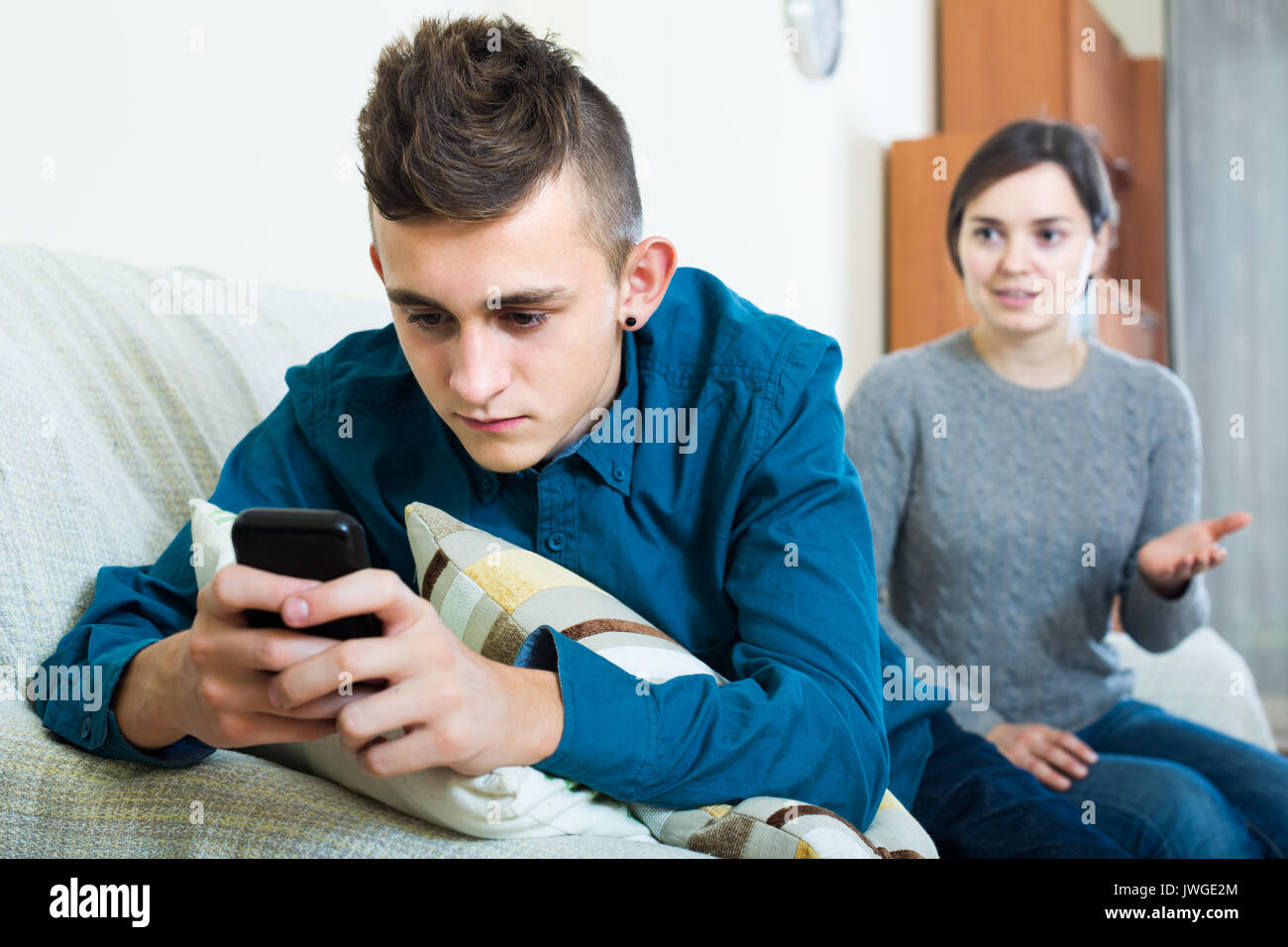 spanish teen age son playing with phone, mother trying to talk Stock Photo
