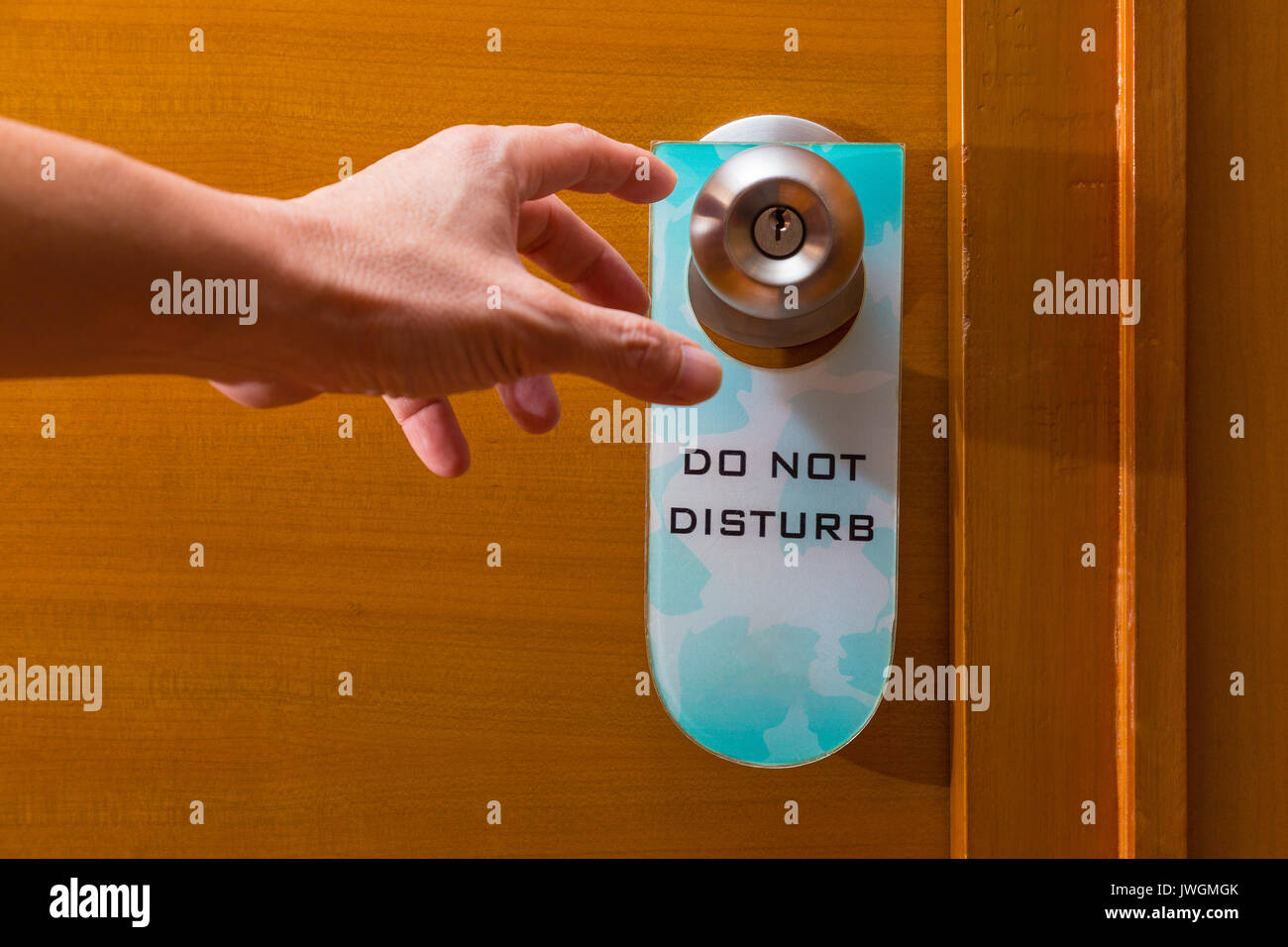 male hand reaching to metal door knob with old Do Not Disturb sign tag haning on, concept of needing privacy or privacy about being intruded Stock Photo