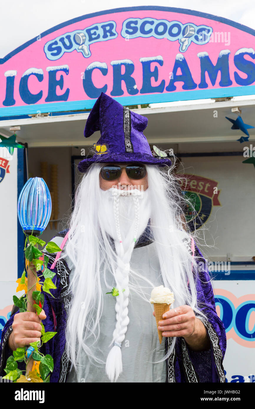 Burley, Hampshire, UK. 12th Aug, 2017. New Forest Fairy Festival. Masses of fairies and elves, sprinkled with fairy dust, descend on Burley for the weekend for a magical enchanting festival in the New Forest. Man dressed as Wizard in robe and hat with long white hair and beard holding stave in one hand and ice cream in the other. Credit: Carolyn Jenkins/Alamy Live News Stock Photo