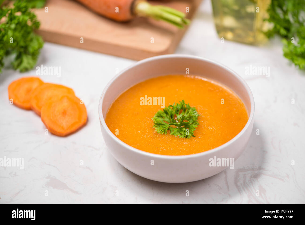 Carrot soup with cream and parsley on white stone background. Top view ...