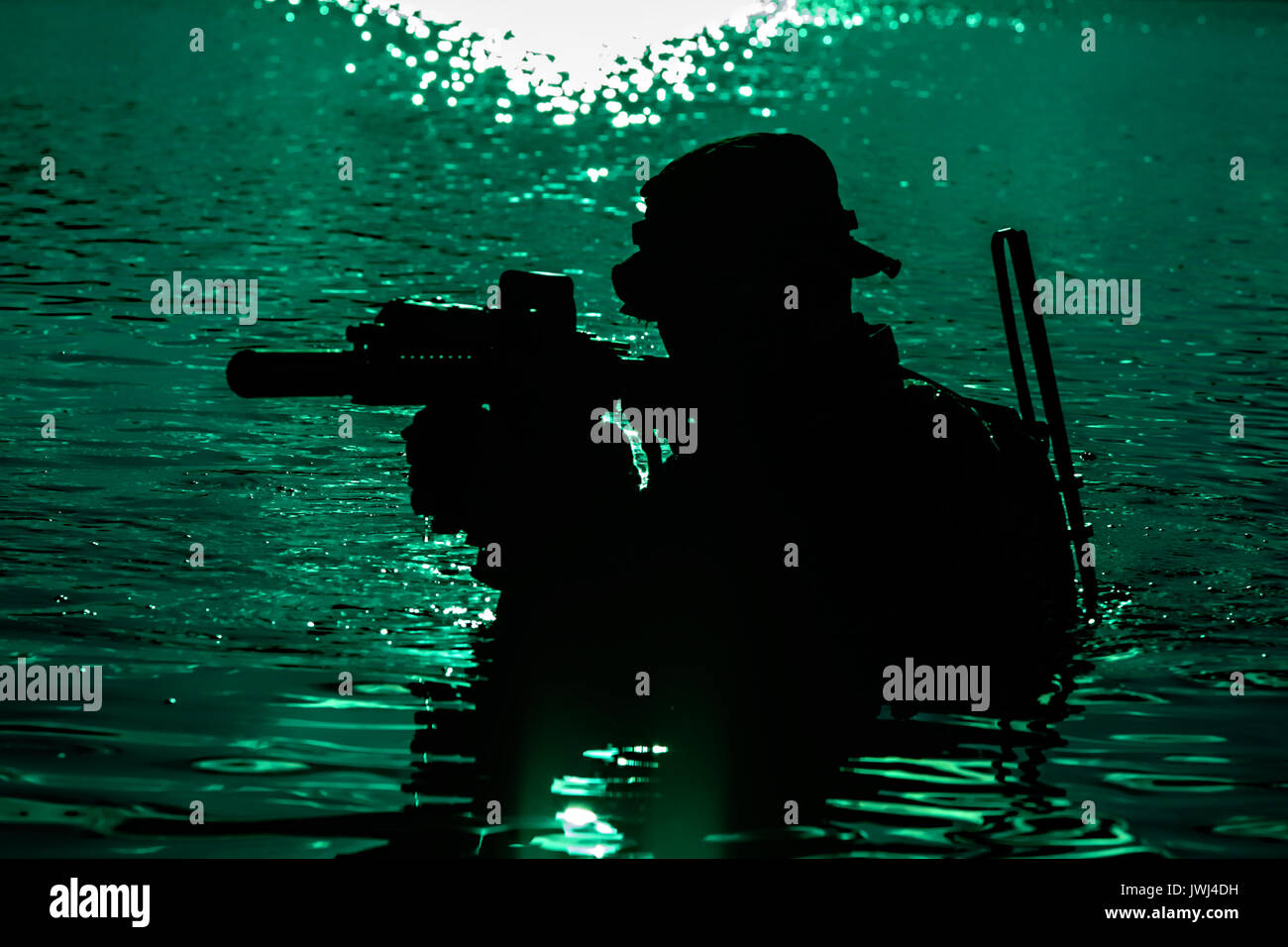 Silhouette of special forces with rifle in action during night raid crossing river in the jungle waist deep in the water. Moon path glowing Stock Photo