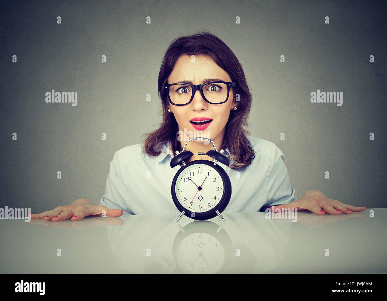Anxious woman picking from under the table with alarm clock. Time