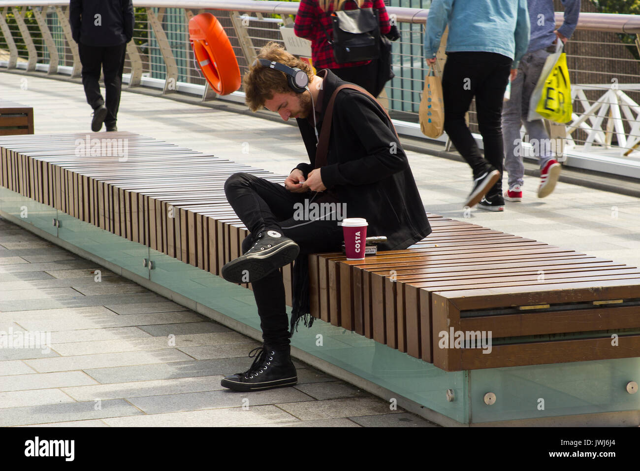 A young man using his mobile phones while relaxing on the waterside at Belfast's River Lagan. Stock Photo