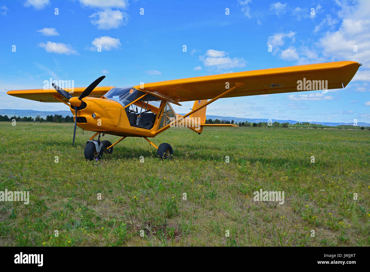 Light sport yellow airplane stands on grass against a blue sky Stock Photo