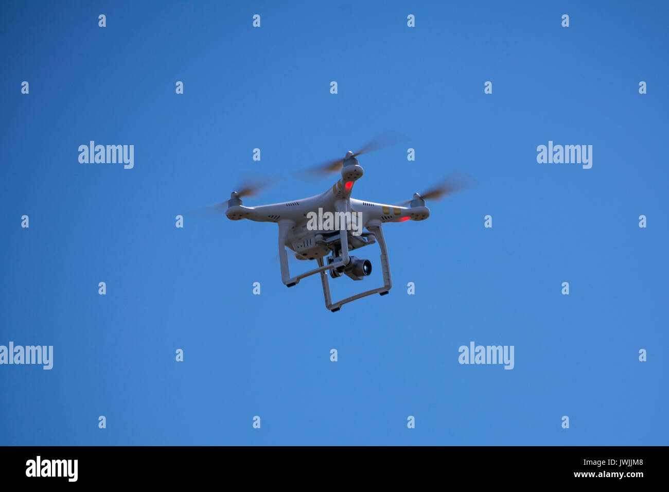 White drone equipped with video camera hovering in mid air. Flying drone with camera Stock Photo