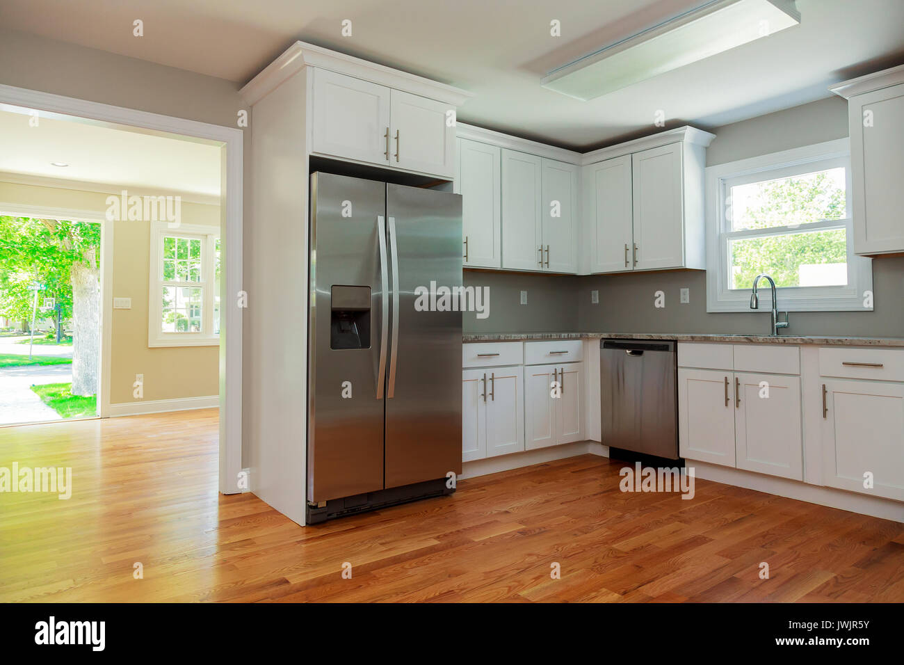 White kitchen interior with sink, cabinets, and hardwood floors in new luxury home with lights off Stock Photo