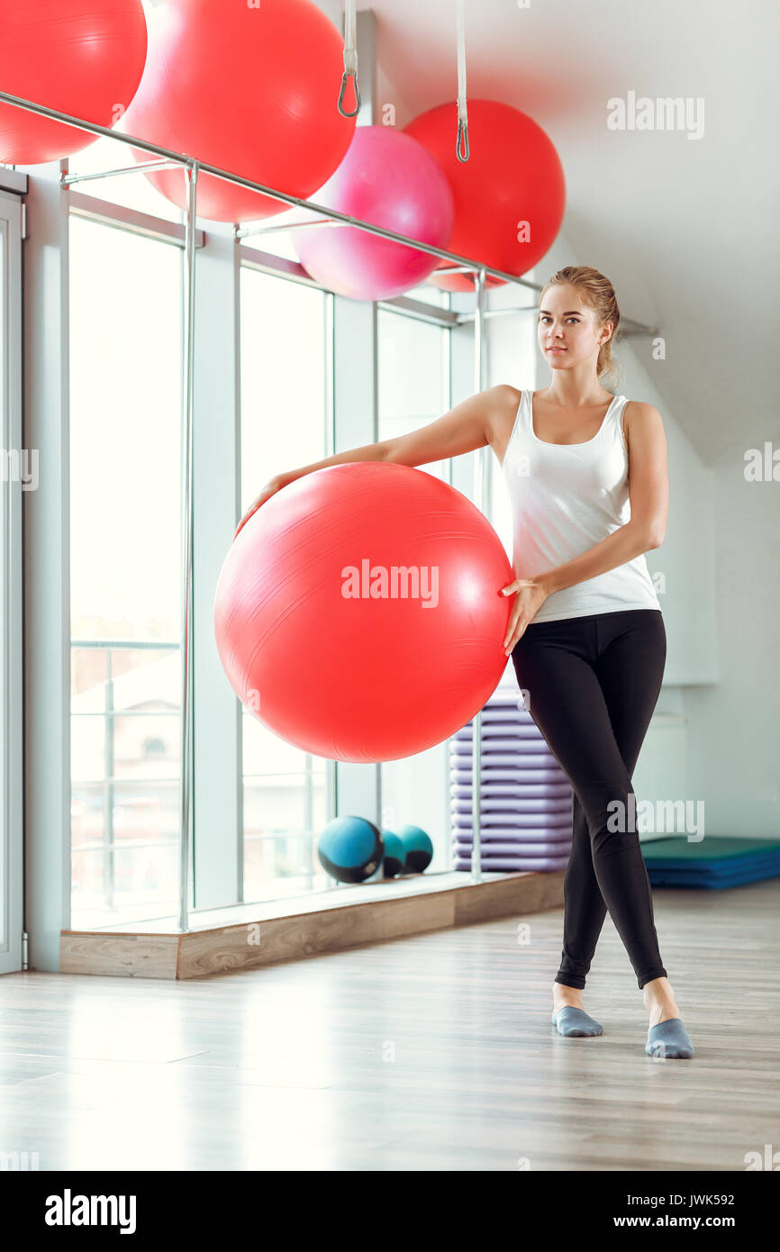 Young athletic woman doing exercises with red fitness ball in the gym