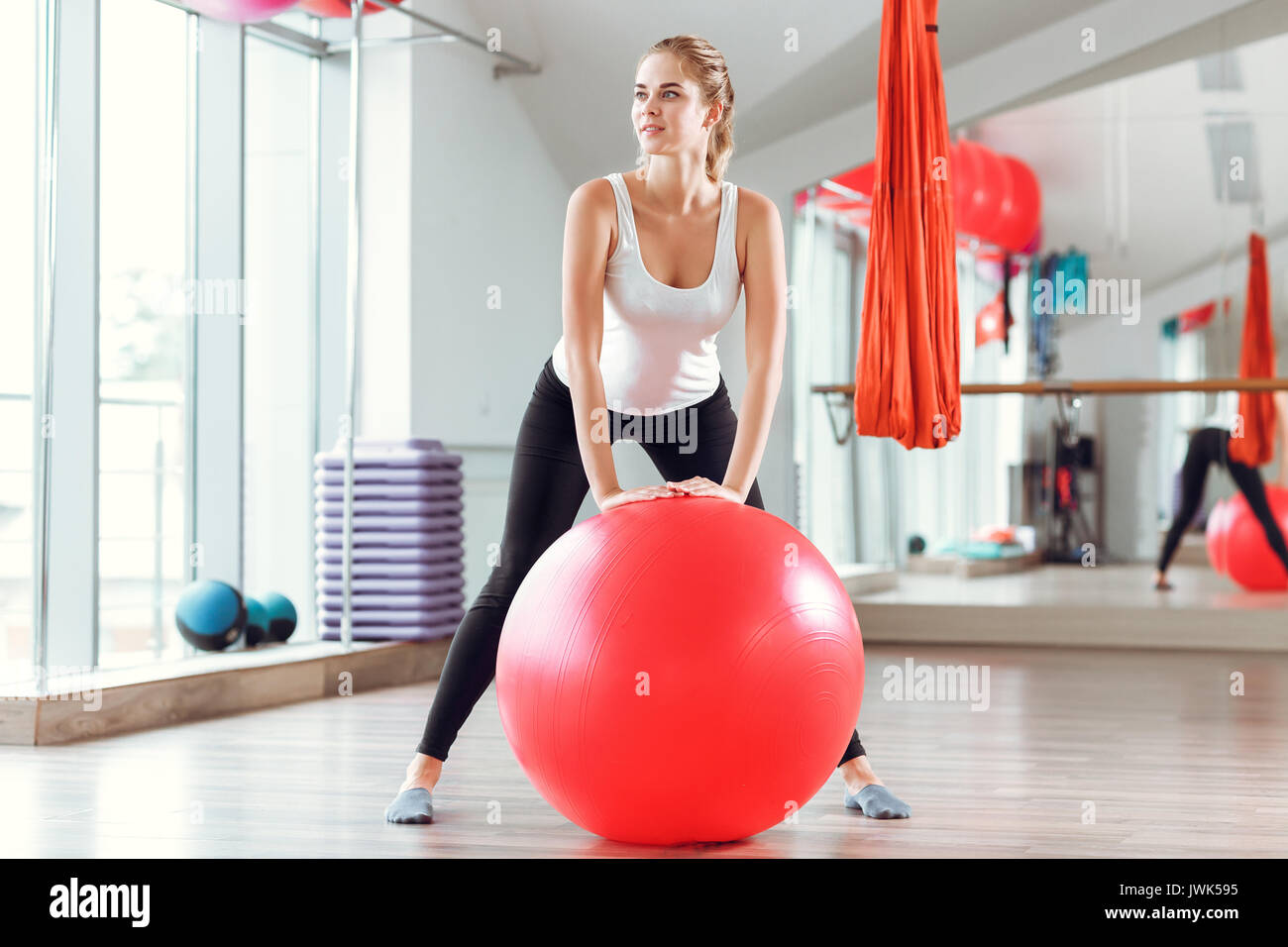 Young athletic woman doing exercises with red fitness ball in the gym