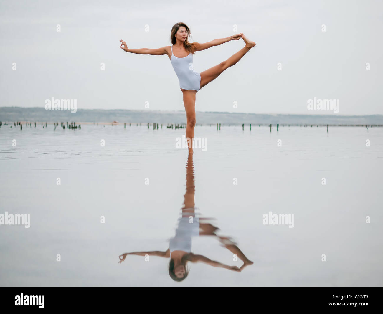 Young caucasian woman in swimsuit practicing yoga in water liman, lake