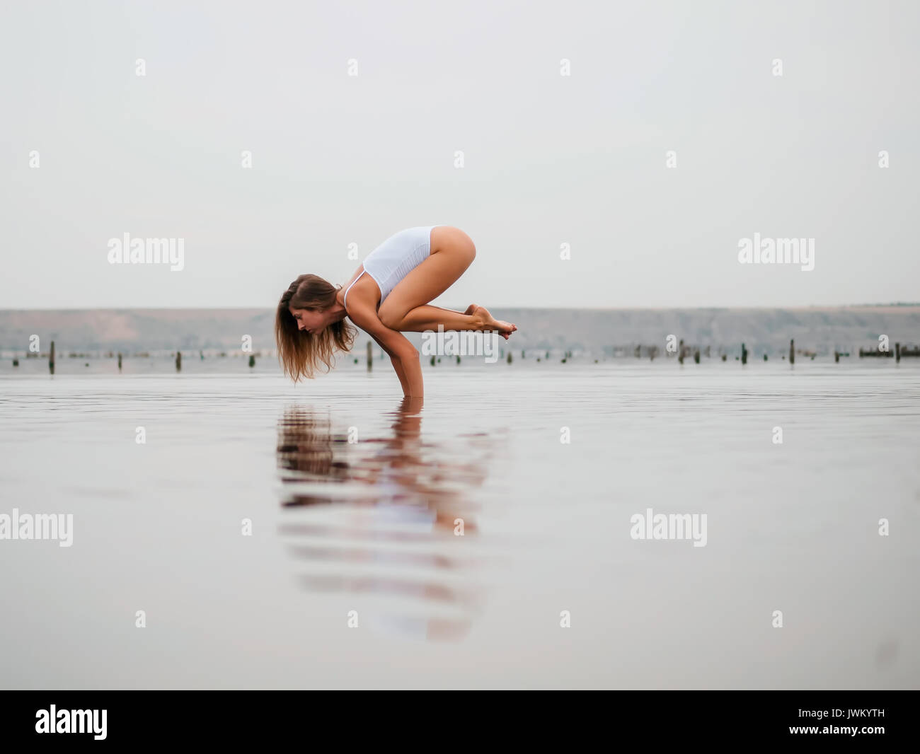 Young caucasian woman in swimsuit practicing yoga in water liman, lake