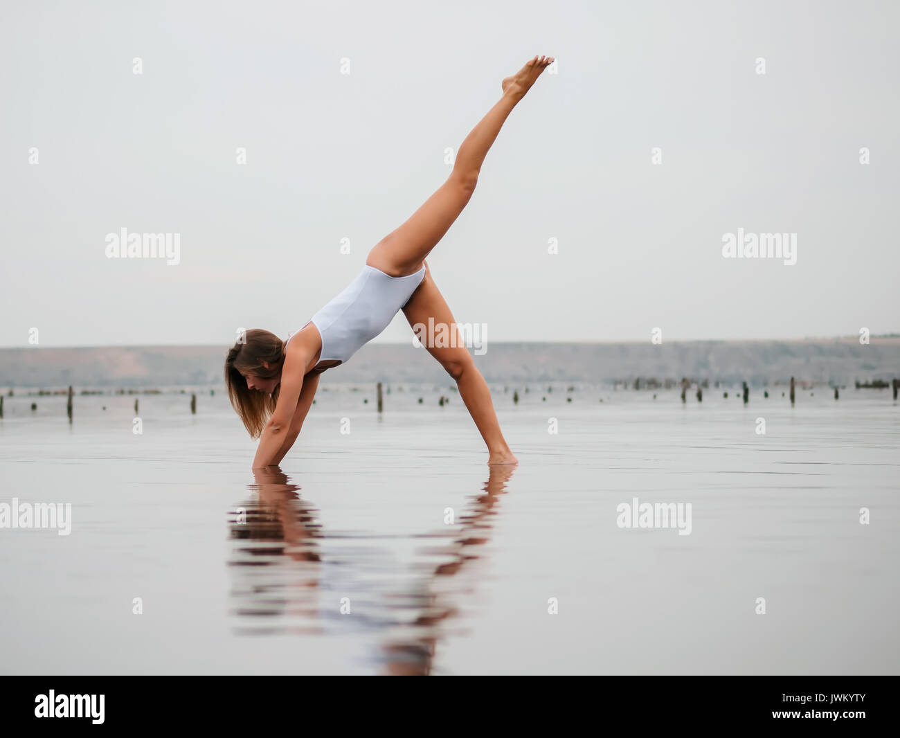 Young caucasian woman in swimsuit practicing yoga in water liman, lake