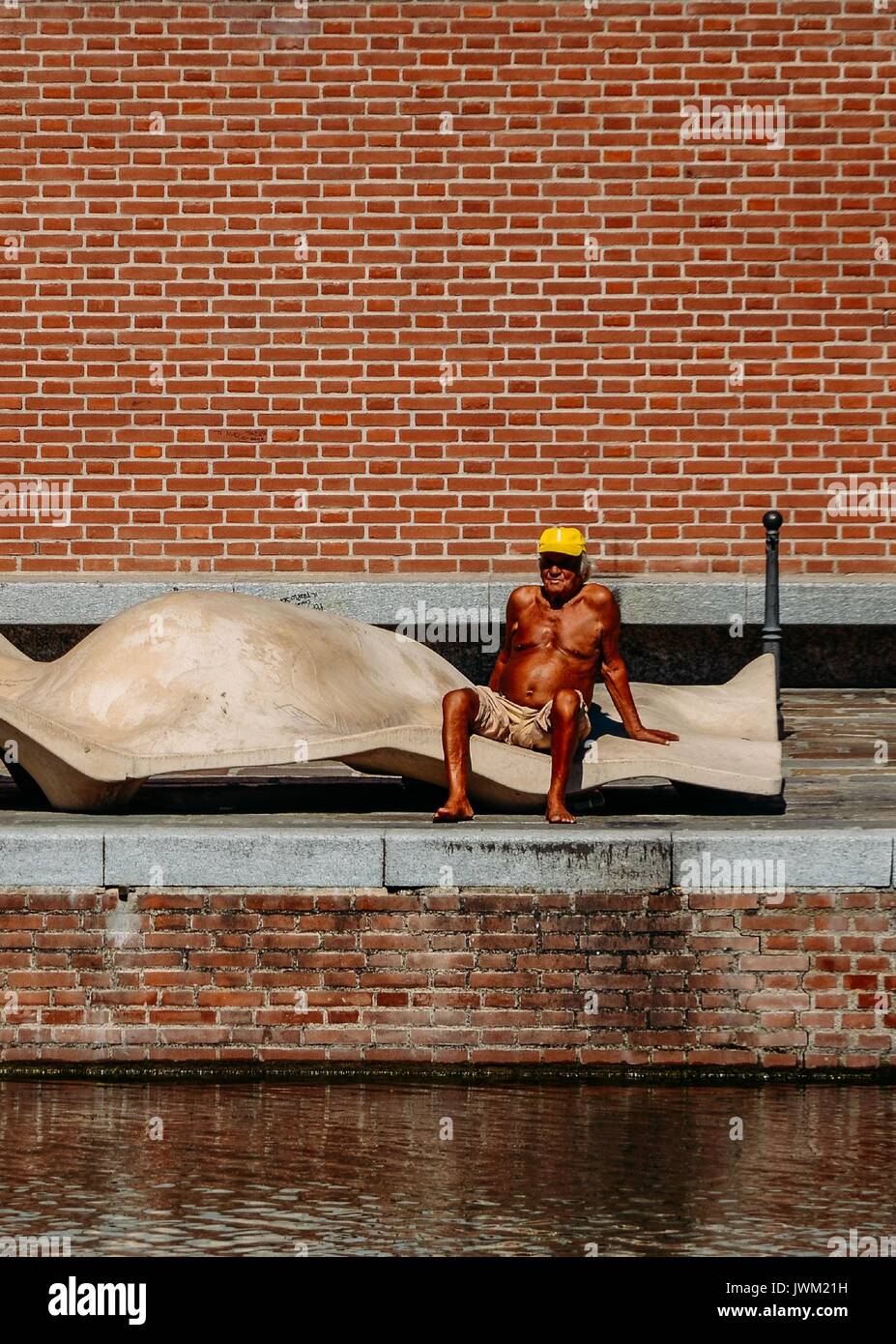 Man (60-65) tanning outside at water's edge in Milan, Italy during the height of the summer Stock Photo