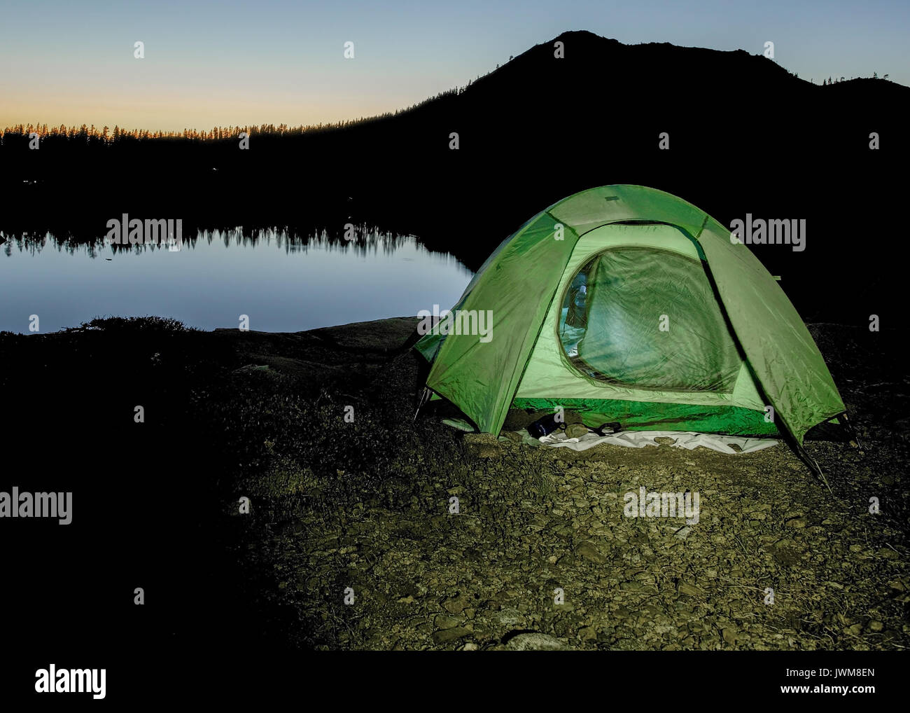 Sunrise by green tent set in the Sierra Nevada overlooking Island Lake, California, featuring the rugged terrain and warm light, to illustrate the con Stock Photo